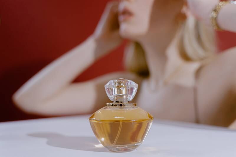Frasco de perfume dourado com mulher branca e loira atrás