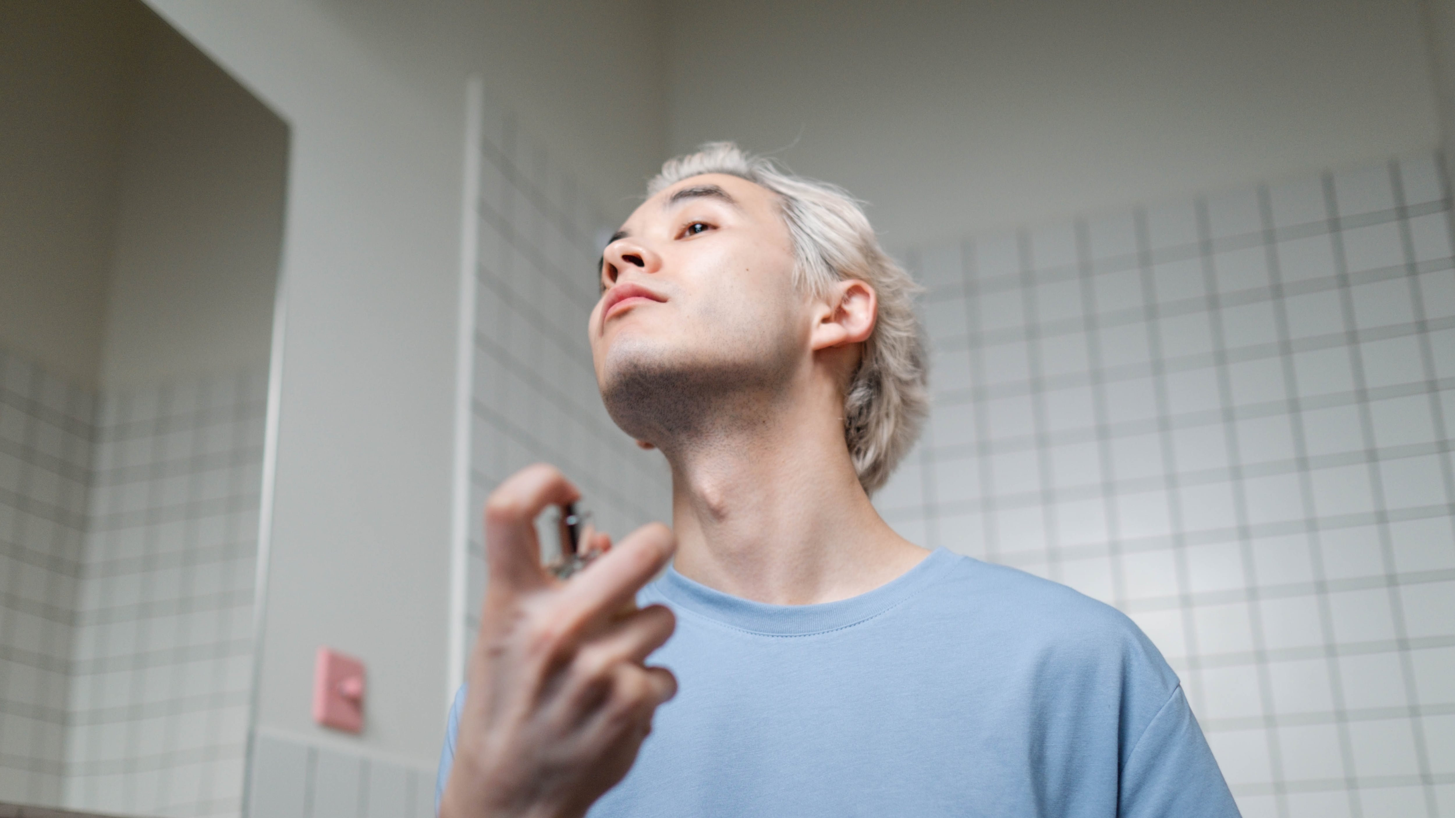 Homem loiro de camisa azul borrifando perfume no pescoço
