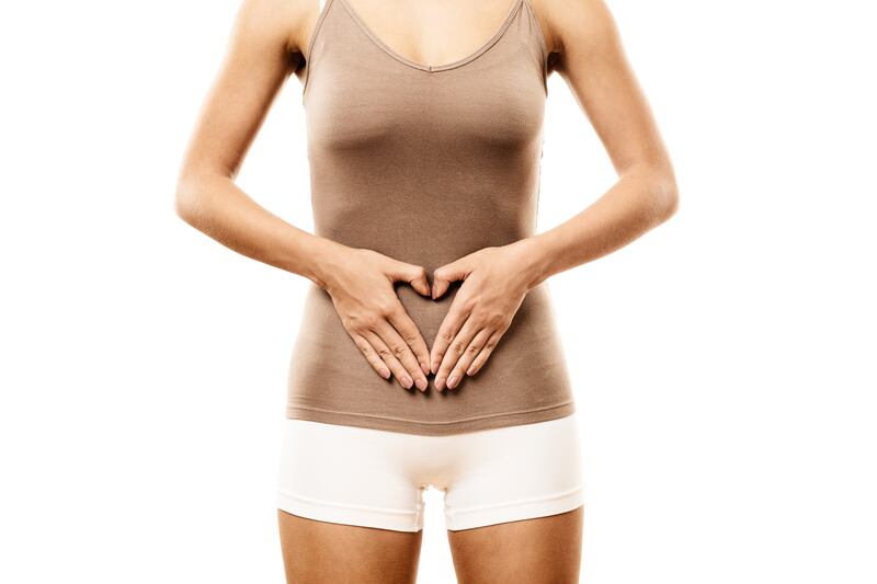 Mulher com blusa marrom e short branco com a mão na barriga